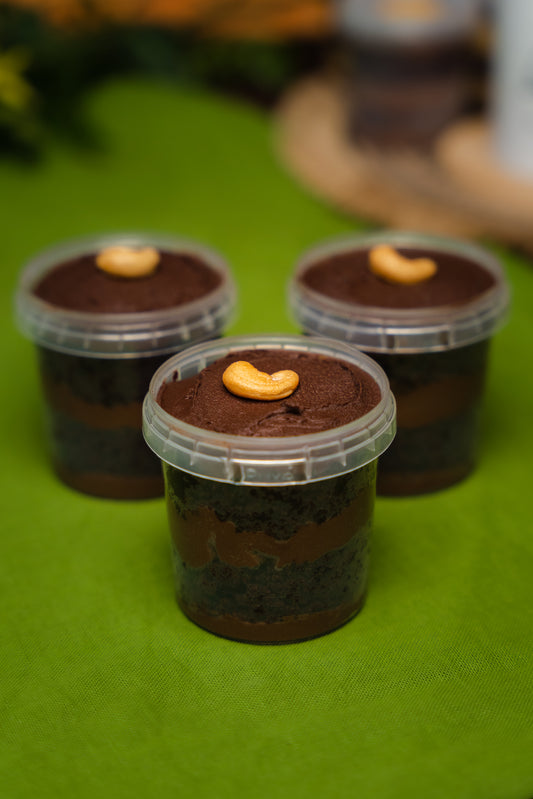 3 chocolate cake in a plastic jar displayed in a green mat. with a cashew ornament