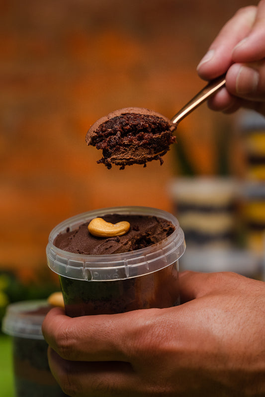 A hand holding a copper spoon, spooning a chocolate mousse cake from a plastic jar  