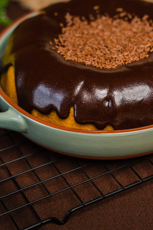 Pound carrot cake cover with a lot brigadeiro, sitting at green dish with brown detailing above a cooling rack  