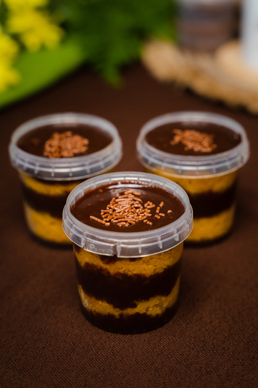 Carrot cake layered in a plastic jar with brigadeiro, topped chocolate sprinkles, displayed on a brown mat 