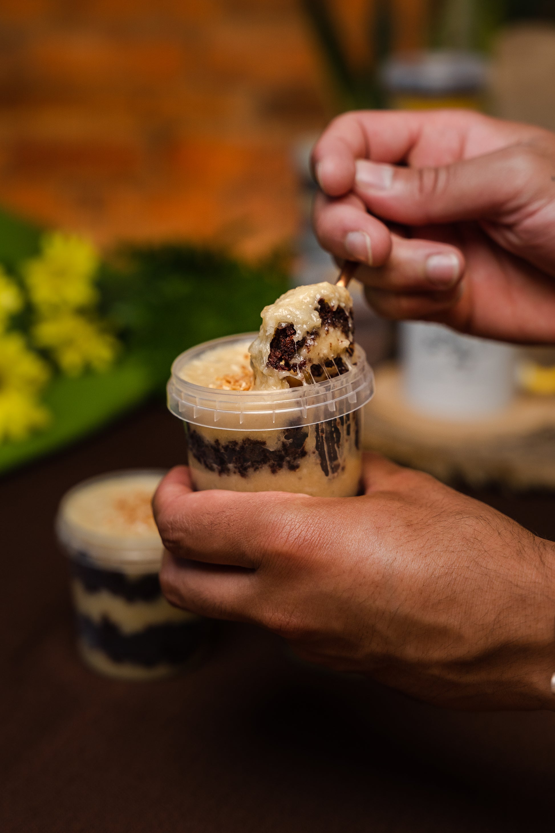 chocolate jar cake layered with coconut brigadeiro (beijinho), topped with toasted coconut flakes, hand holding and spooning with copper spoon   