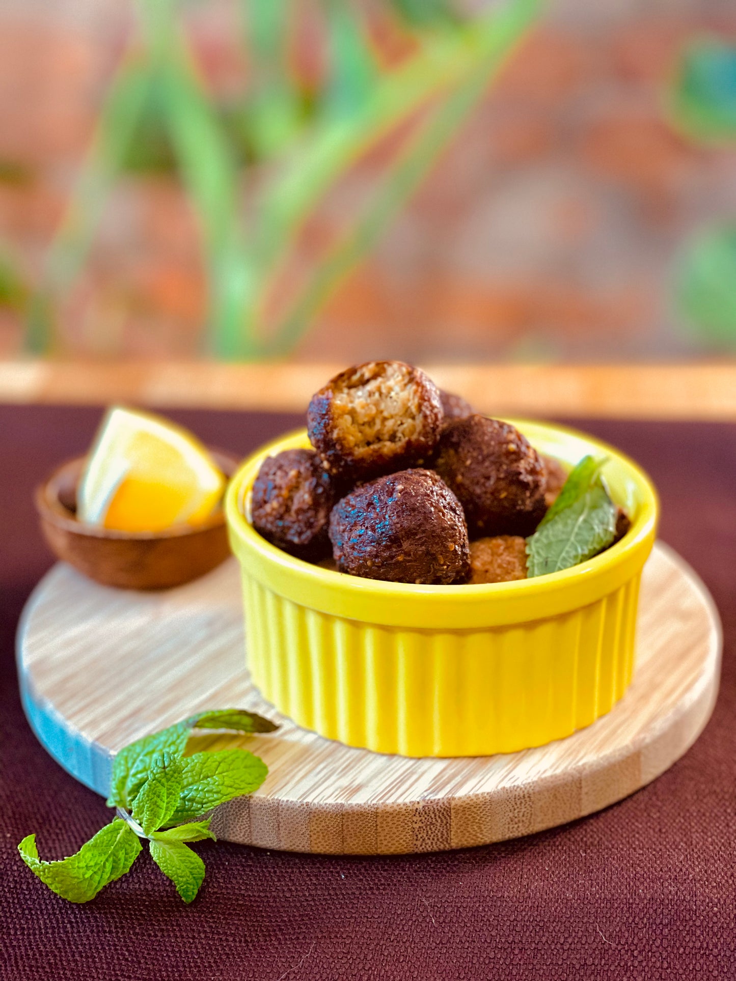 Kibbeh inside a yellow bowl, on top of a wood board, mint is garnish, green plant on the background 