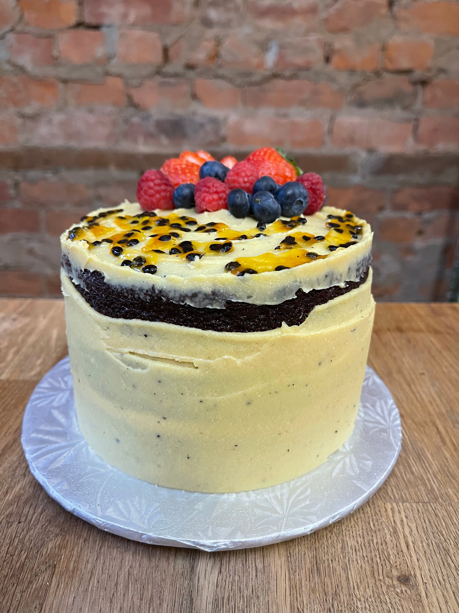 Chocolate cake, filled with passion fruit brigadeiro, half naked with passion fruit brigadeiro topped with blueberries, strawberries and raspberries display in silver board 